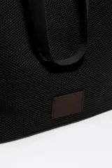 Bolso shopper de estructura blanda y gran tamaño, confeccionado en tejido técnico tipo mesh. Cuenta con doble asa de hombro, cierre mediante cordón ajustable y etiqueta de cuero con logo grabado en la parte frontal.