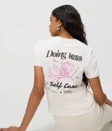 Remera de algodón con cuello redondo, mangas cortas y estampa en la espalda con diseño de un perro descansando en una reposera y la frase "Doing less is Self Care".