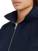 Cortavientos azul marino con cuello alto, cierre de cremallera, dos bolsillos con botones, detalles distintivos de Tommy Hilfiger y logo gráfico bordado en el pecho.