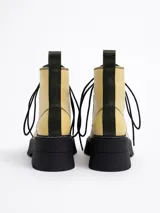 Botín acordonado de cuero color amarillo pastel con pespuntes negros, plataforma track negra y tirador trasero.