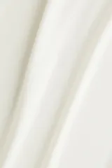 Top sin mangas color blanco hueso, de tejido liso y corte ajustado, con cuello alto tipo mock neck y bordes sin rematar.