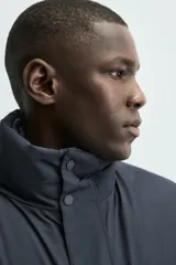 Parka acolchada impermeable color gris oscuro, de corte regular fit, con cuello doble subido, bolsillos de vivo en la cadera y cierre frontal con cremallera oculta por solapa con botones a presión.