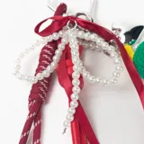 Llavero decorativo con mosquetón metálico en forma de corazón, que incluye una variedad de elementos colgantes: una pieza tejida a crochet con forma de sandía, una tira de perlas, cintas de raso rojas y cordones deportivos con punteras metálicas.