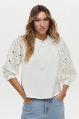 Blusa blanca con mangas abullonadas de broderie, cuello elevado con volados y detalles de volados en los hombros.