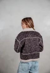 Campera de gamuza con estampado animal print en tonos grises, forrada con corderito sintético en color crema. Presenta cierre frontal con botones tipo toggle y detalles de costuras visibles.