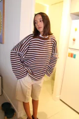 Sweater de punto oversize con diseño de rayas horizontales en color marrón y blanco. Presenta cuello redondo, mangas largas caídas y un parche pequeño con texto en el puño.