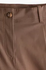 Pantalón de corte holgado color marrón, de estilo sastrero, con cintura clásica, trabillas para cinto y cierre con botón y cremallera. Presenta piernas rectas con pinzas frontales y bolsillos laterales.