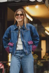 Campera de jean con corte boxy, cuello camisero y cierre frontal. Presenta bolsillos frontales y puños en tejido de punto color vino con detalles bordados.
