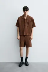 Bermuda de corte relajado color marrón con finas rayas verticales negras. Presenta cintura elástica ajustable con cordón y bolsillos laterales y trasero.