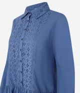 Vestido corto de corte evasé confeccionado en tricolina de algodón, color azul. Presenta cuello camisero, cierre frontal de botones y un panel central con detalle bordado calado. Posee mangas largas con puños abotonados.