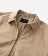 Campera tipo bomber de sarga color beige, con cuello inglés, cierre frontal de cremallera y puños y cintura ajustados con elástico en tono contrastante.