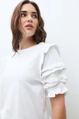 Remera de algodón color terracota con cuello redondo y mangas cortas con detalle de volados escalonados y costuras decorativas.