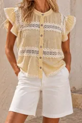 Blusa romántica de color amarillo pastel, confeccionada en tejido liviano con textura arrugada y aplicaciones horizontales de encaje blanco. Cuenta con cuello mao, abotonadura frontal con botones oscuros, mangas cortas con volados y terminaciones de puntilla en el ruedo.