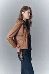 Campera estilo biker confeccionada en cuero ovino, con solapas amplias, charreteras en los hombros y cinturón ajustable en la cintura. Presenta cierres metálicos en el frente y bolsillos laterales, con forro interior de poliéster.