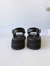 Sandalias negras de cuero con tiras cruzadas, plataforma track y hebilla lateral.