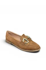 Mocasín de gamuza color beige, con detalle de hebilla metálica dorada en el empeine, costuras visibles y suela plana.
