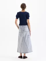 Pollera midi de denim en color azul claro con efecto lavado. Presenta un diseño de corte recto con costuras decorativas visibles, bolsillos frontales tipo cargo y una abertura central en el ruedo.