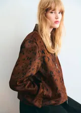 Chaqueta de cuero de potro color marrón con estampado tipo animal print en tonos oscuros, de corte recto y largo recortado. Cuenta con cuello camisero, cierre frontal de cremallera metálica y mangas largas amplias con puños rectos.