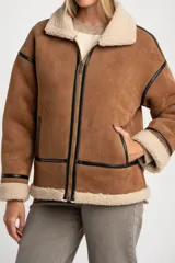 Campera tipo gamulán de corte oversize, confeccionada en material efecto gamuza color camel con interior y detalles de cuello y puños en corderito sintético color crema. Presenta cierre frontal y detalles de ribetes en cuero sintético negro.