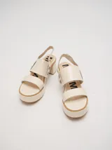 Sandalias de cuero color marrón con plataforma y taco cuadrado. Presentan dos tiras anchas sobre el empeine y una tira trasera con elástico. Decoración de doble argolla en los laterales.