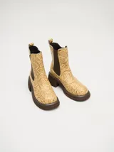Botas estilo Chelsea de cuero texturizado en color beige claro con estampado floral estilo tooling, con elásticos laterales marrones, plataforma y taco ancho oscuro.