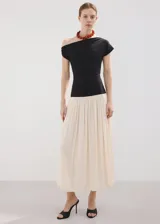Vestido largo de diseño asimétrico con cuerpo negro entallado de cuello barco y manga corta, combinado con una falda larga evasé en color beige claro.