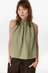 Blusa verde militar de lino italiano, con corte en línea A y hombros al descubierto. Presenta escote halter con frunces, cuello con volado y lazo en la espalda.
