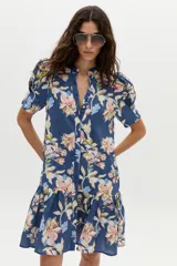 Vestido corto azul de lino con estampado floral en tonos rosados, beige y celestes, cuello mao con escote en V, mangas cortas abullonadas, botones frontales ocultos y volado en el ruedo.
