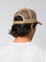 Gorro trucker de color verde militar, con visera curvada marrón claro, panel frontal rígido y red trasera. Cuenta con un parche circular bordado en la parte delantera y cierre ajustable snapback.