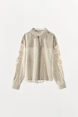 Camisa de corte recto confeccionada en mezcla de algodón y viscosa, con estampado de rayas verticales. Presenta cuello solapa, cierre frontal con botones y mangas largas con aplicaciones de encaje y bordados a tono.