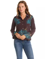 Camisa de crepe con estampado floral en tonos verdes y marrones, cuello con solapa, cierre frontal con botones y detalle de mostacillas bordadas en los hombros. Presenta mangas largas con terminación amplia.