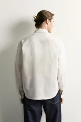 Camisa relaxed fit de algodón con estructura, cuello solapa, manga larga con puño abotonado, bolsillo de parche en el pecho y cierre frontal con botones. Presenta diseño de rayas finas.