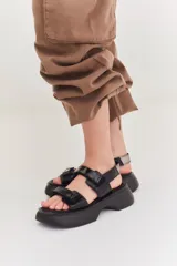 Sandalias de plataforma con suela de goma negra y tiras de cuero sintético color beige con cierre de velcro ajustable.