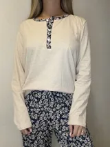 Pijama de algodón compuesto por una remera de manga larga en color beige melange con escote redondo, cartera de botones y detalles de tela floreada en el cuello y tapeta, y un pantalón largo con estampado floral en tonos azules.