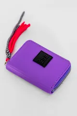 Billetera violeta con cierre de cremallera y tirador de cordón multicolor. Tiene un aplique cuadrado negro con letras blancas.