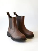 Bota tipo Chelsea de cuero color chocolate, con paneles elásticos laterales, tirador trasero y suela track negra de goma.