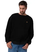 Buzo de cuello redondo confeccionado en tejido sherpa negro, con textura suave y elástica. Presenta puños y banda inferior en tejido acanalado y una pequeña etiqueta con el logo de la marca en el pecho.