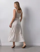 Falda larga de poliéster color beige con finas rayas verticales. Presenta una pretina ancha elastizada con efecto smock y volados en los ruedos de los tres paños que componen la falda.