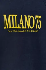 Sudadera de tejido de punto color azul marino, con cuello redondo y mangas raglán. Presenta un estampado frontal en amarillo con el texto "MILANO 75" y una dirección debajo.