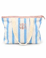 Tote bag amplia con estampado de ondas en tonos azules y verdes, asas largas de color beige, cierre superior con borde rosado y logo bordado en el centro.