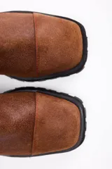 Botin de cuero vacuno color suela, con diseño de caña media, doble cierre lateral y suela track negra de goma.