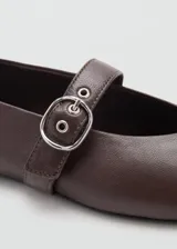 Zapato plano estilo Mary Jane color marrón, confeccionado en piel de ovino, con punta fina y tira en el empeine con hebilla metálica plateada.