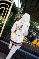 Campera con capucha de color crema, con diseño estampado en la espalda que incluye un caballo y la frase The Winter Carousel. Presenta bandas laterales con inscripciones en las mangas y un borde inferior con franjas horizontales en tonos bordó y celeste.