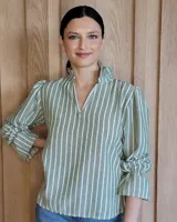 Blusa de algodón con estampado de rayas verticales blancas y verdes. Presenta cuello alto con volados, escote en V y mangas largas con puños elásticos y detalle de volados.