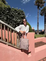 Bolso tipo tote bag de símil cuero color rosa pálido, con asas dobles y detalles de costura en color beige claro. Presenta un bolsillo frontal rectangular aplicado y herrajes metálicos.