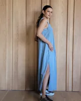 Vestido largo de denim azul, con escote en V, sin mangas, corte holgado, bolsillos laterales y aberturas en los costados de la falda.