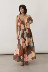Vestido midi de tirantes ajustables con lazo en los hombros, escote en V y diseño amplio con estampado floral abstracto en tonos marrones, rosados, celestes y amarillos.