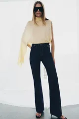 Jeans de tiro alto con corte flare y ajuste slim. Presenta trabillas en la cintura, bolsillos delanteros con detalle de botones metálicos y raya planchada a lo largo de las piernas. Cierre frontal con cremallera y botón.