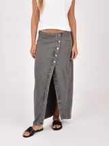 Falda larga de denim gris con diseño cruzado y cierre frontal mediante botones metálicos. Presenta un tajo central que aporta movimiento y un estilo moderno.