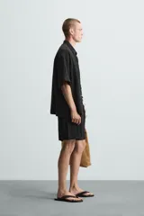 Bermuda negra de corte regular, confeccionada en tejido jacquard con efecto arrugado. Presenta cintura elástica ajustable con cordón blanco, bolsillos laterales y bolsillos traseros de vivo.